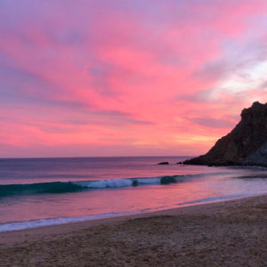 A wave gently crashing on Burgau beach, under a vibrant pink and purple sunset.